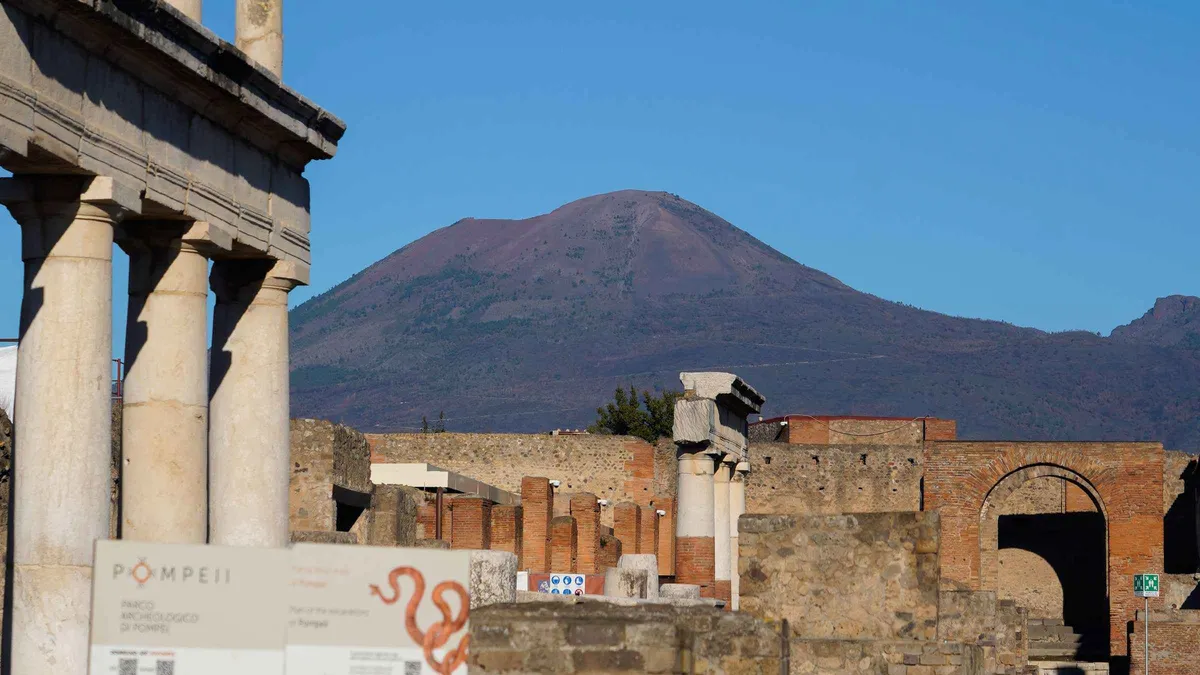 A guided group walking a paved Roman street between brick shop fronts in Pompeii, the tour on the Pompeii skip-the-line train ticket and guided tour from Sorrento, Campania, Italy